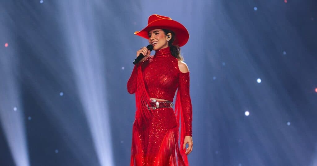 Paula Fernandes aparece durante a gravação de seu DVD, usando chapéu e roupa vermelha.